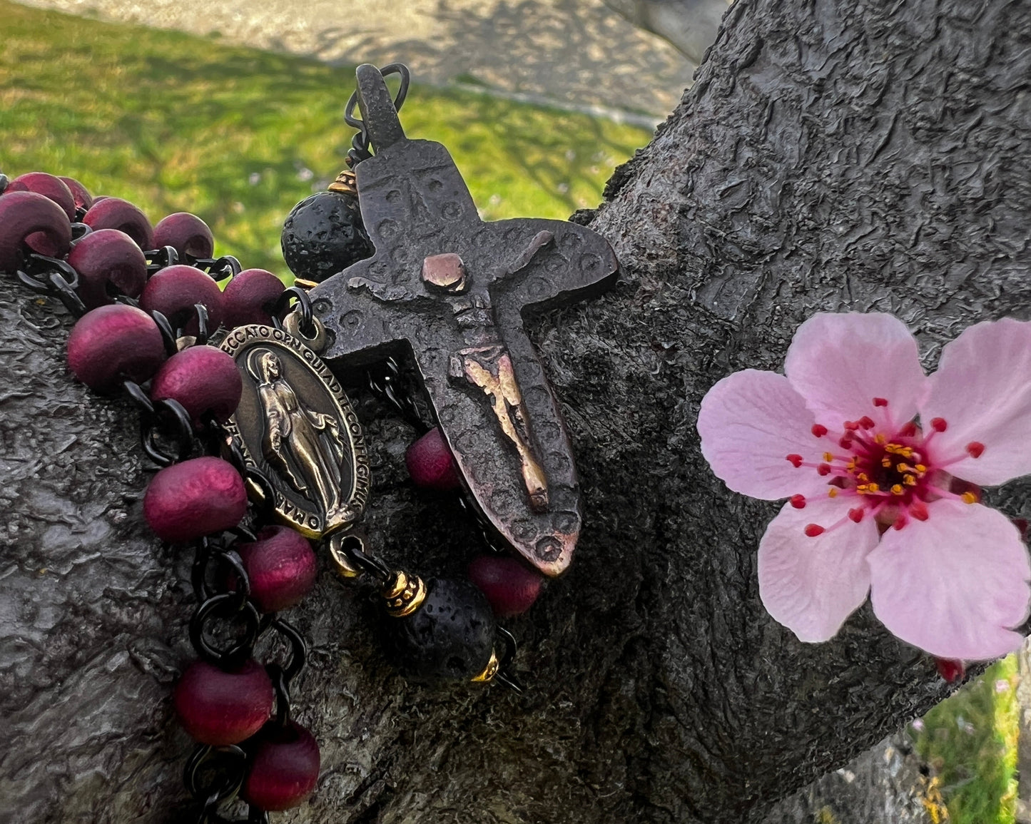 Rosary with a pink flower attached to a tree trunk