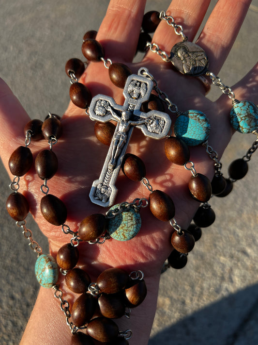 Close-up of a rosary with brown beads and a silver cross held in a hand.